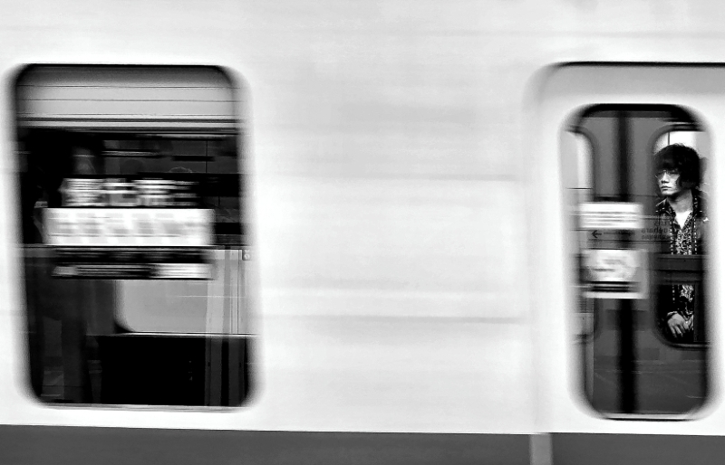 Metrô em alta velocidade com um passageiro com características orientais na porta, olhando para o lado de fora